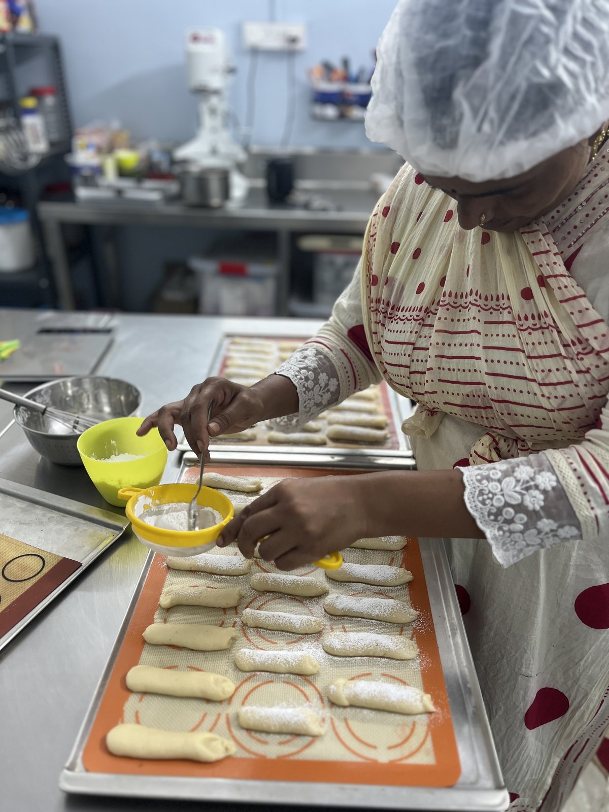 Piping rows of ladyfinger sponge onto a lined baking tray in the studio kitchen