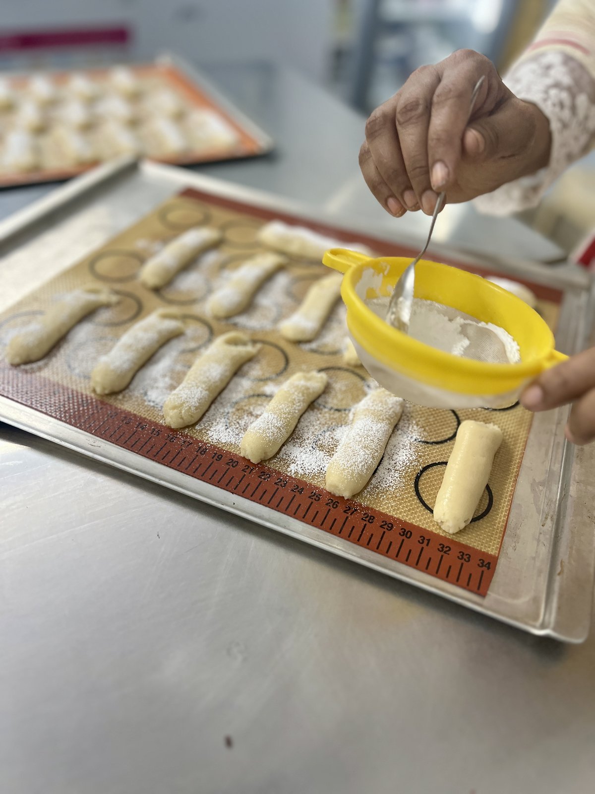 Dusting icing sugar through a sieve over piped ladyfinger sponge before it goes into the oven
